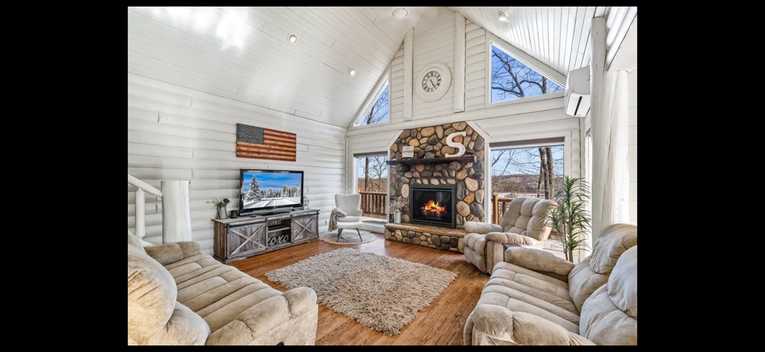 Bright vaulted living room with stone fireplace and large windows